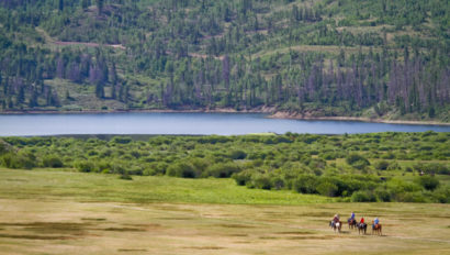 Group of people riding horses toward a lake