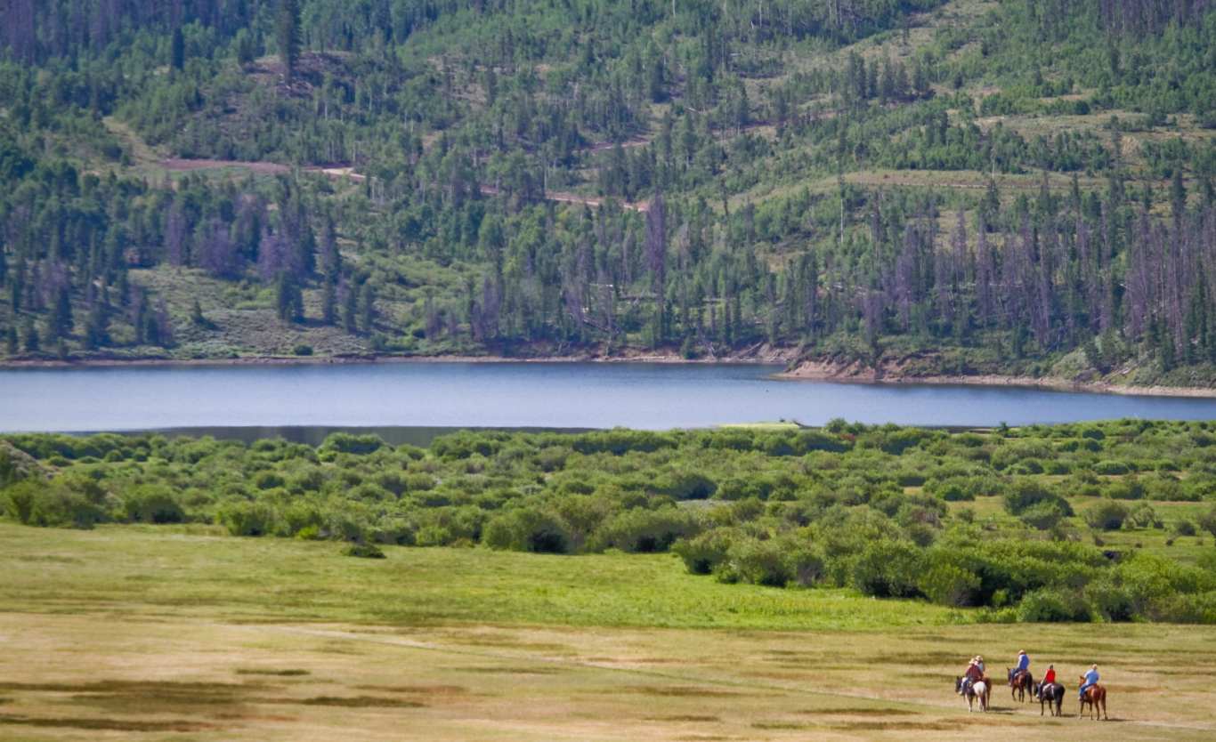 Group of people riding horses toward a lake