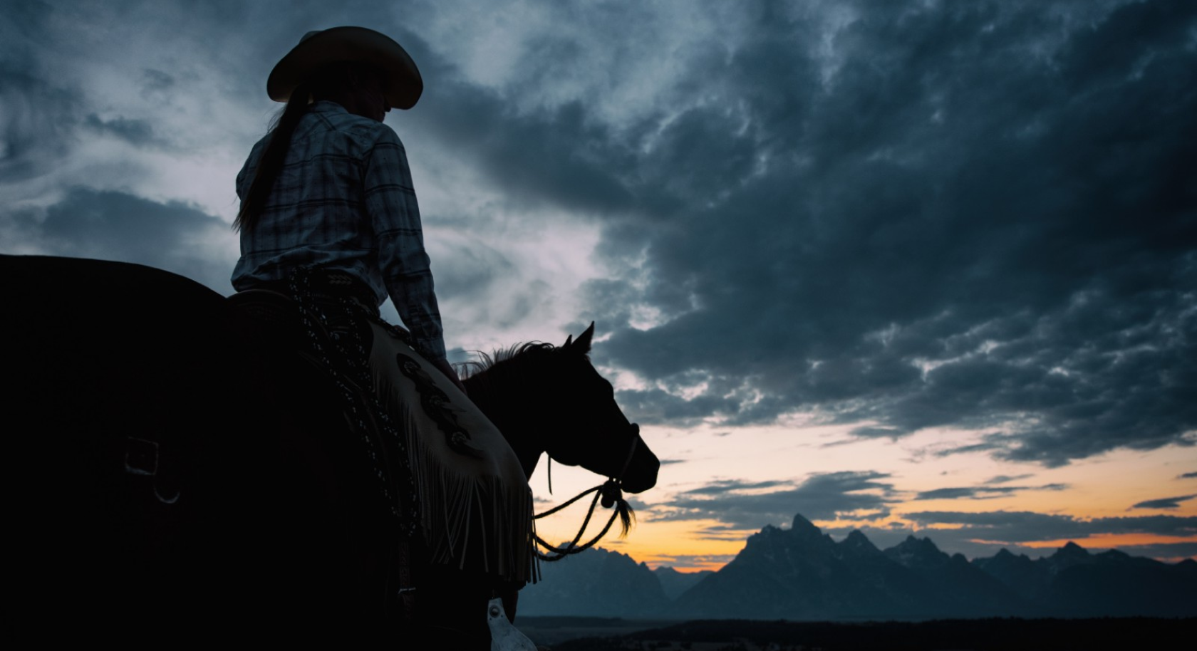 Woman on a horse looking out at the mountains at sunset