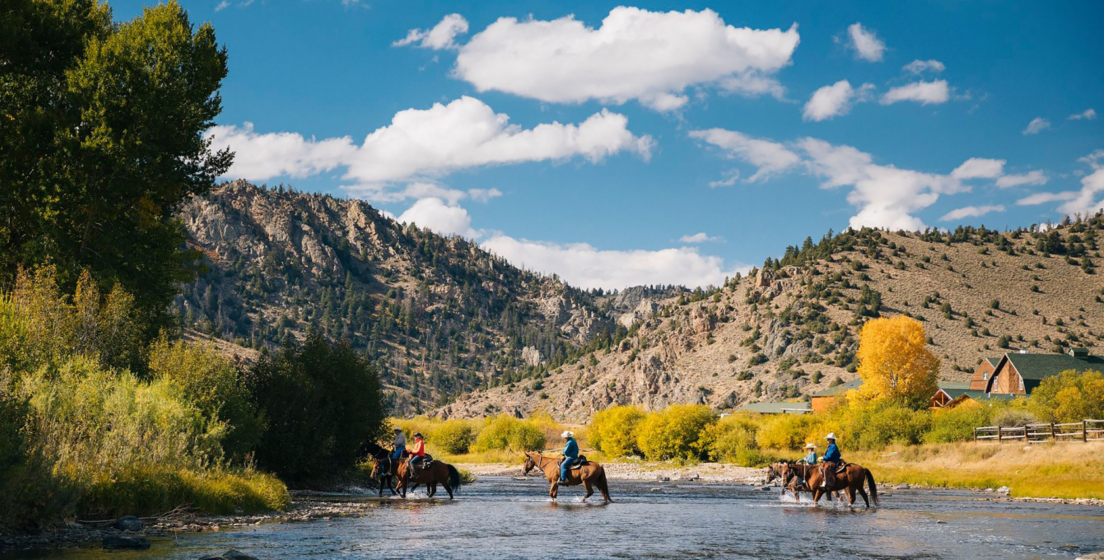 Group of people riding horses across a river