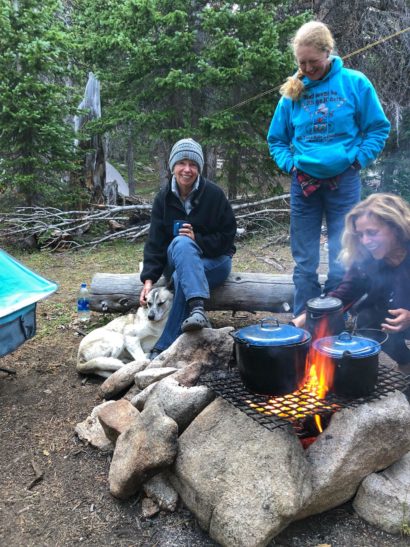 three women and dog around campfire cooking