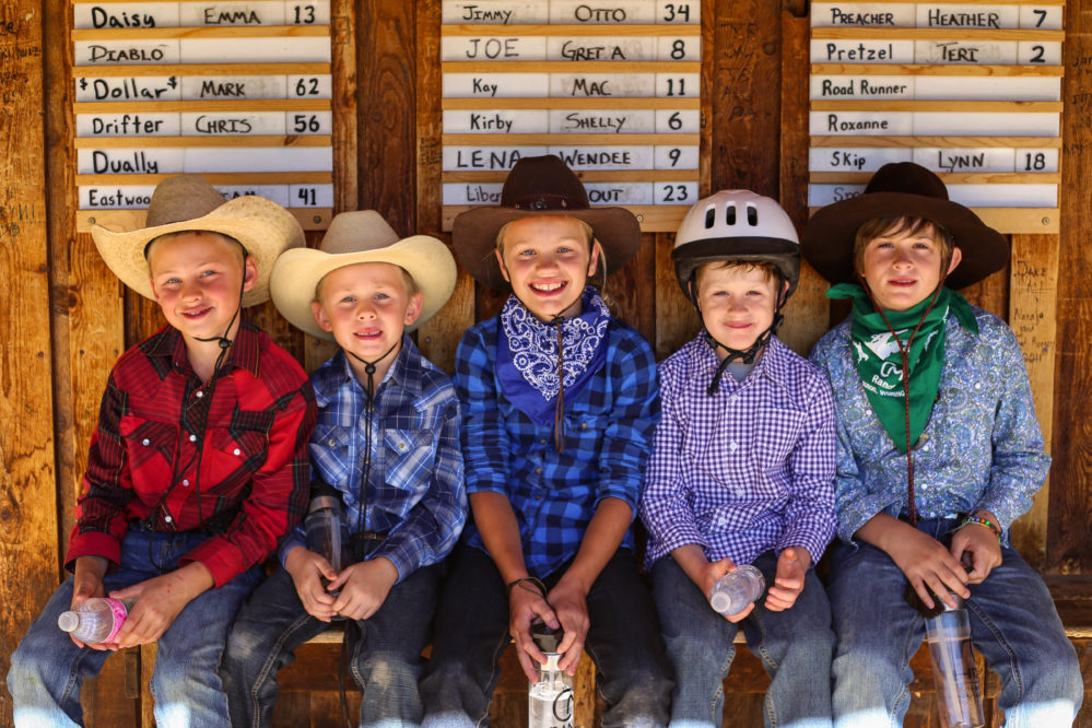 5 kids sitting on barn porch with cowboy hats and helmets