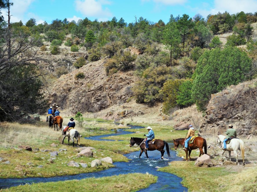 group of riders crossing stream in canyon