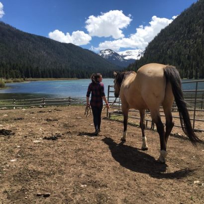 lady leading horse to water with mountains in the background