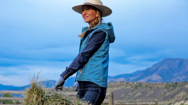 Woman in cowboy hat and jacket carrying a bale of hay