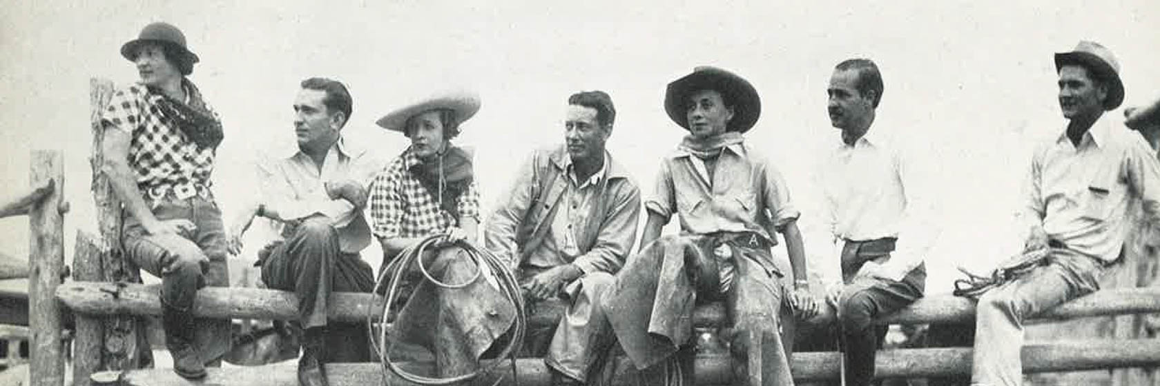 Old photo of guests in cowboy gear sitting on a fence