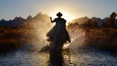 Rider on horse splashing into a creek at sunset