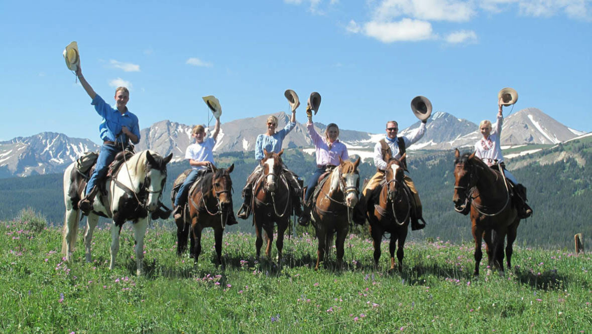 A family on horses raising their hats at Covered Wagon Ranch