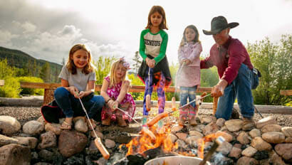Group of kids roasting hot dogs over a camp fire at Rawah Ranch