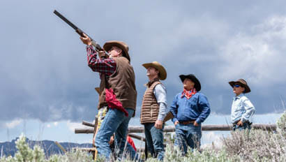Three men watching one man shoot a rifle at Triangle C Ranch